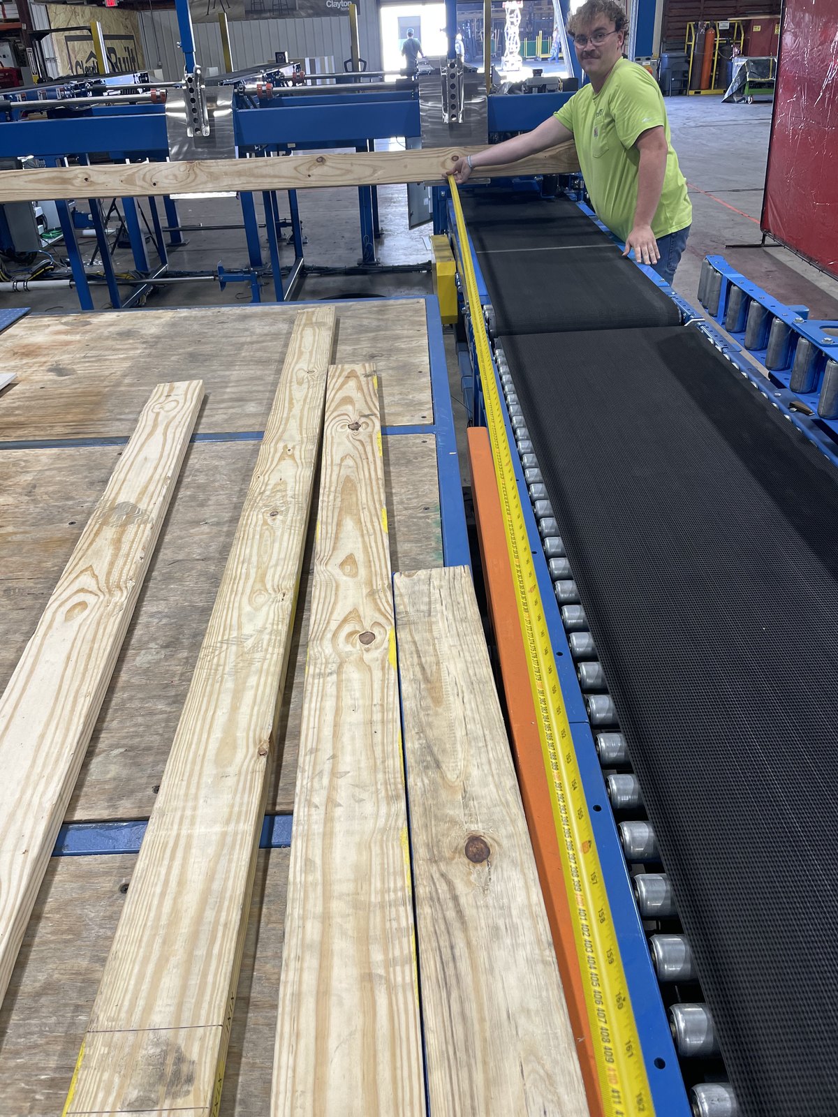 Lumber boards staged on the powered conveyor with an operator alongside the line