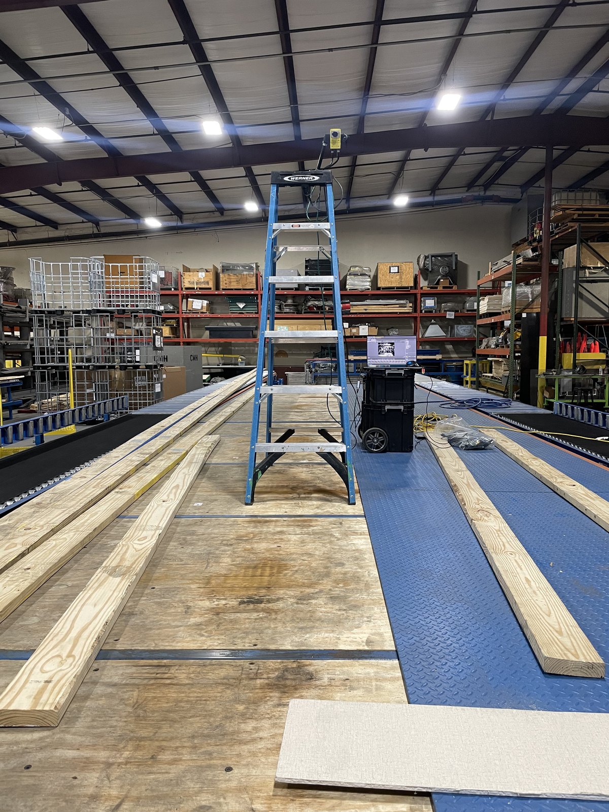 Wide view of the floor assembly line with gantry rails and lumber staged along the conveyor