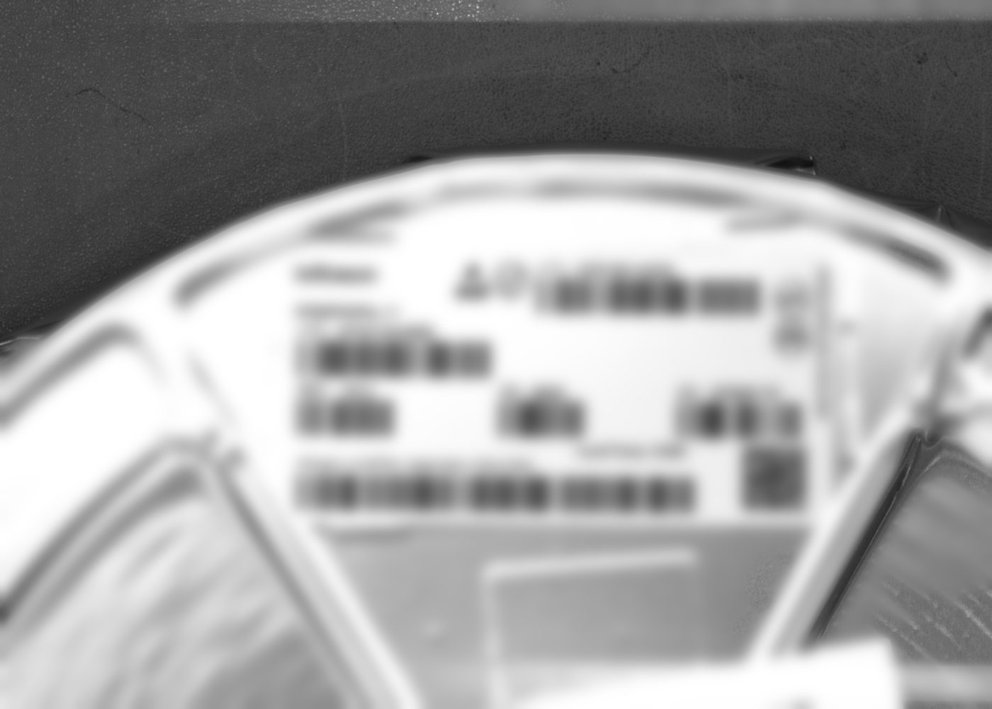 Component reel with a supplier label near the outer edge, captured in monochrome by the inspection camera; label text blurred