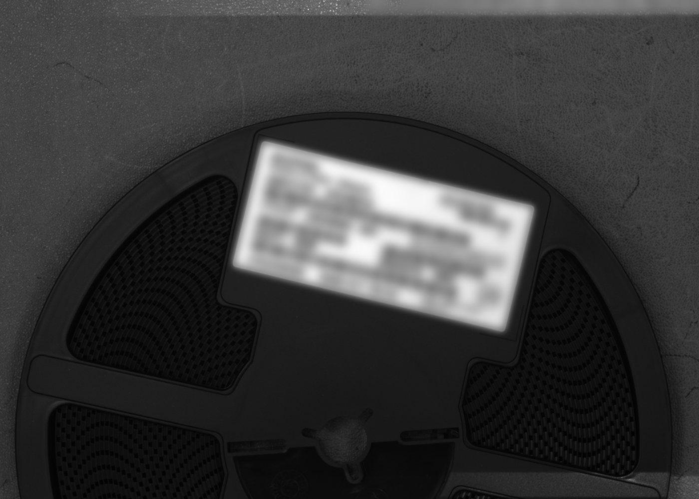 Dark component reel with a small bright label off to one side; label text blurred